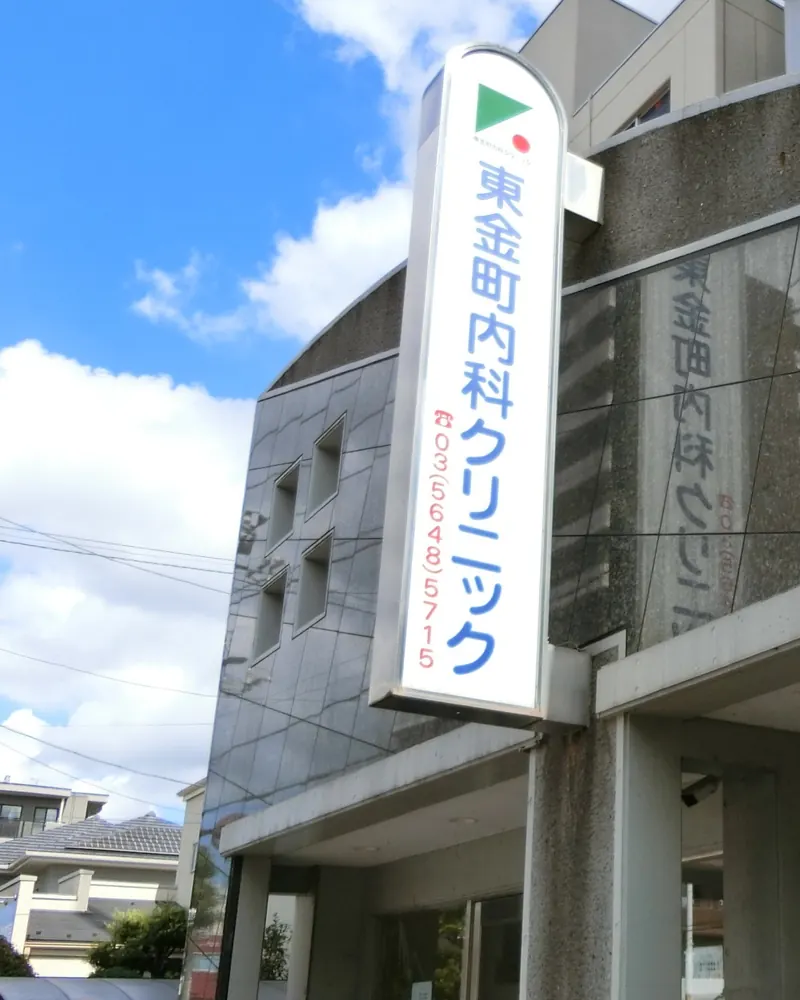 東金町内科クリニックの外観。建物の前に、緑の三角と赤い丸のマークが入った縦長の看板が立っている